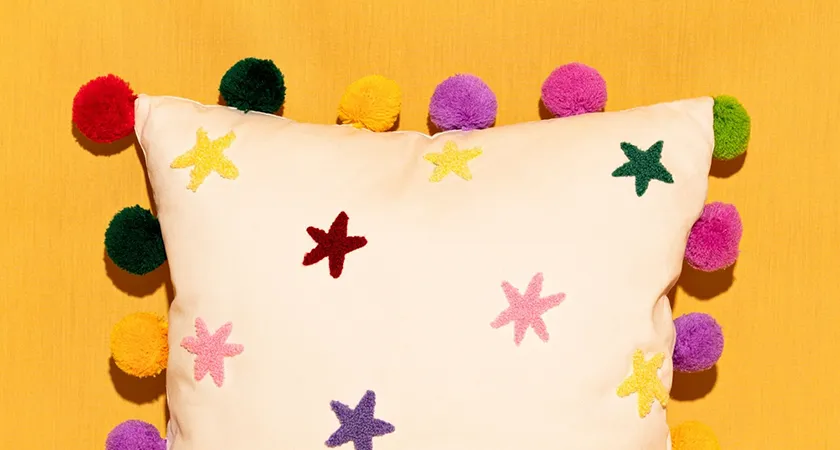 colourful pom pom cushion on yellow background