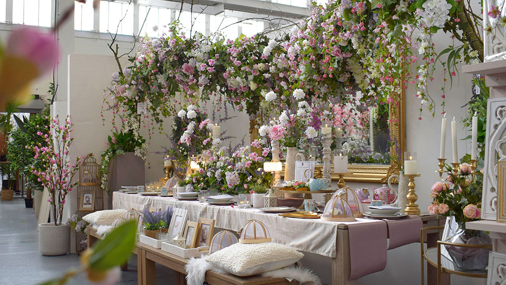 long table with bridgerton-inspired pastel faux floral display, artificial blossom trees and floral arch, golden mirror, and accessories