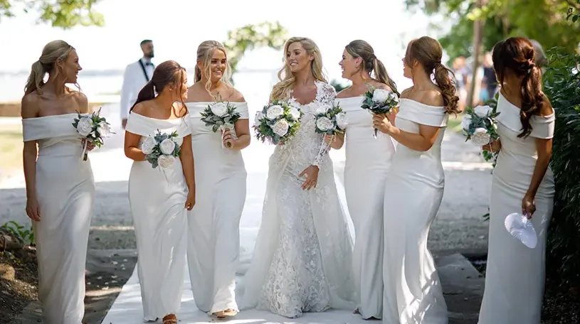 bride and bridesmaids holding white faux wedding flowers while walking outside